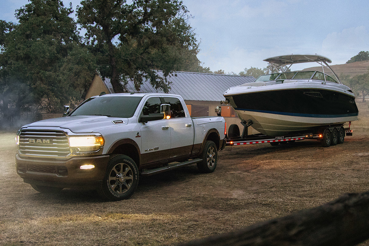 The 2020 Ram 2500 parked on a dirt parking lot in a suburban area while towing a boat