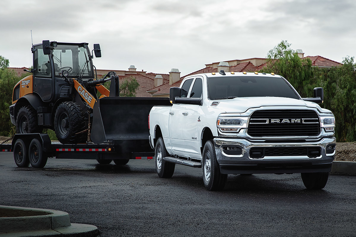 Ram 2500 blanc tirant un engin de terrassement sur une remorque dans un quartier résidentiel.