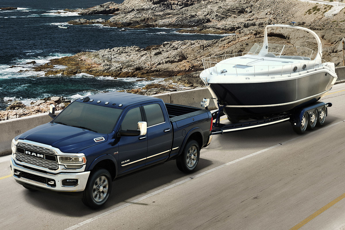 Un Ram 2500 bleu descend une côte avec des montagnes rocheuses en arrière-plan tout en tirant un petit bateau sur une remorque.