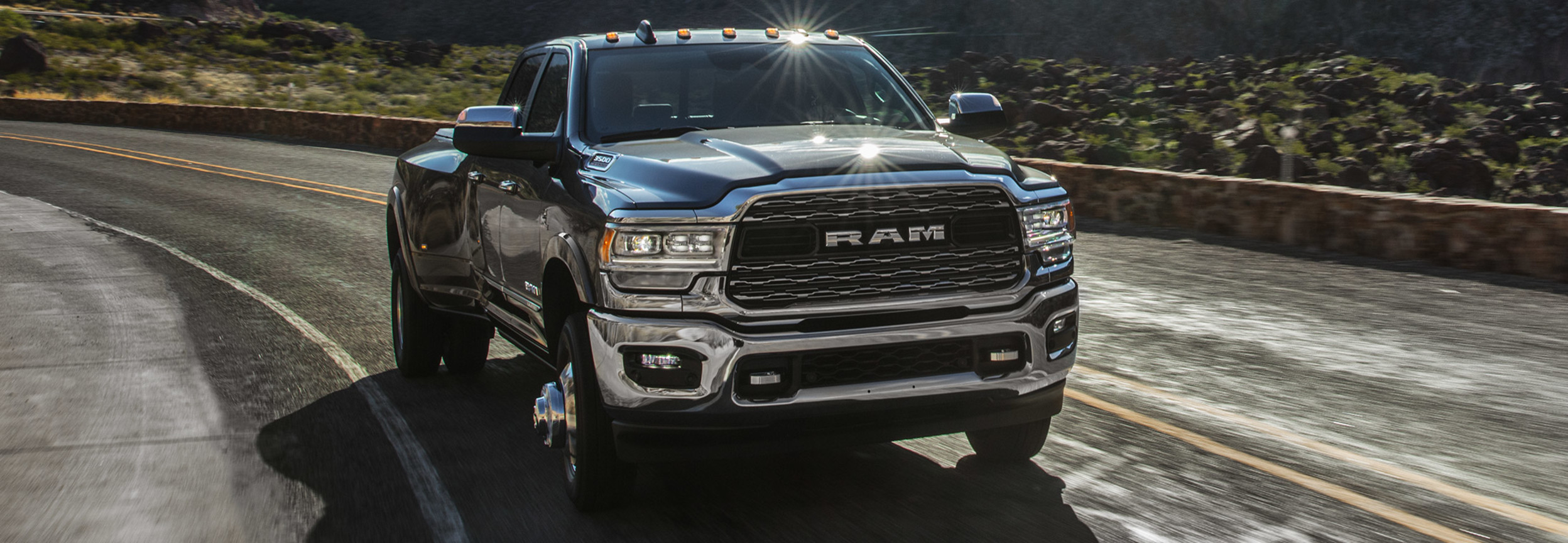 A black RAM 3500 driving down a road with mountains in the background