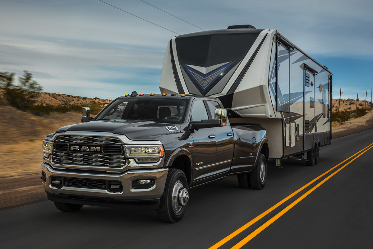 Black 2020 Ram 3500 hauling a large grey & black trailer down the road.