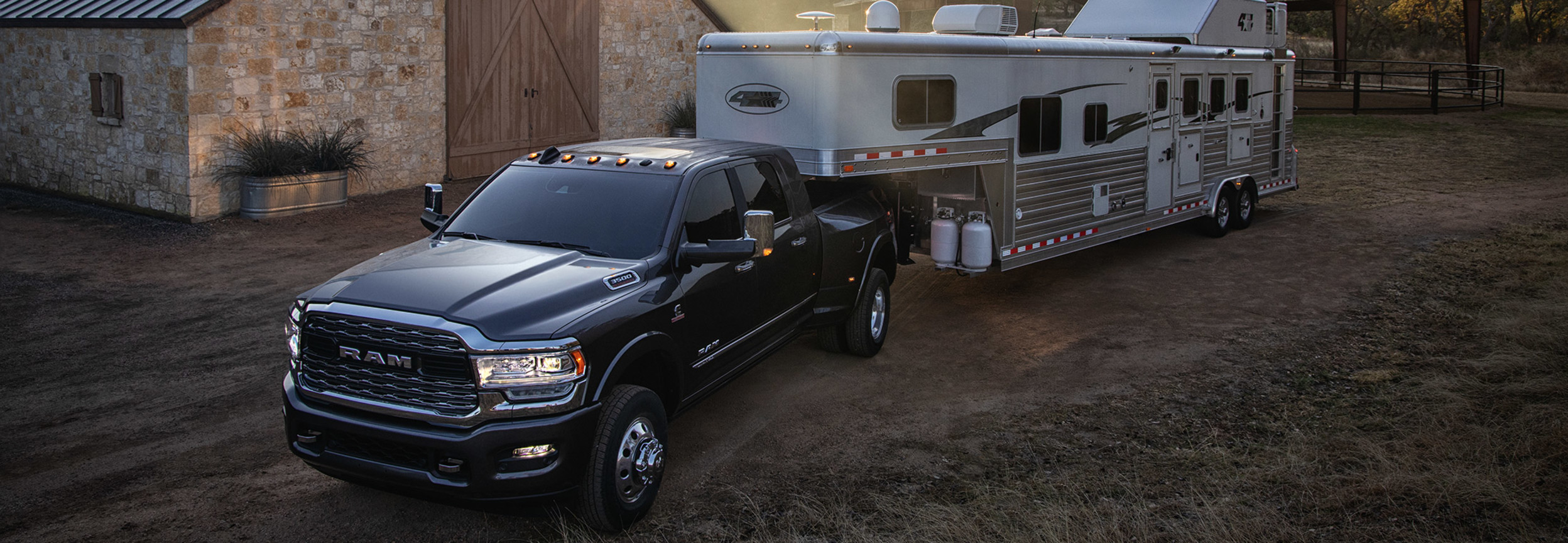 An overhead view of a large camping trailer hitched to a Diamond Black Crystal Pearl coloured 2021 Ram 3500. Farm buildings are in the background.