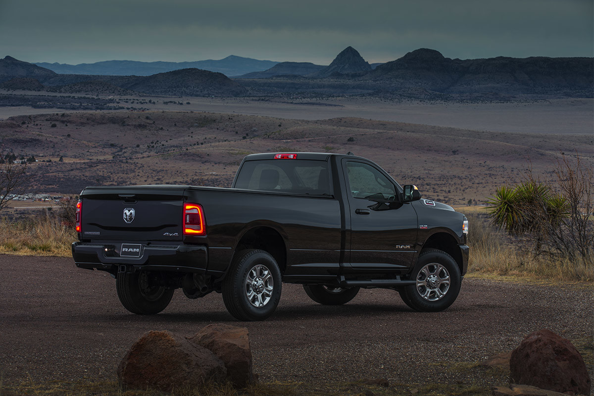 A side view of a Diamond Black Crystal Pearl coloured 2021 Ram 3500 parked on a road with a desert vista in the background.
