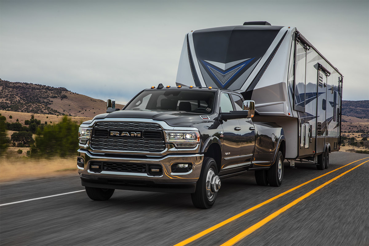 A front view of a Walnut Brown Metallic coloured 2021 Ram 3500 towing a camper trailer on a road through the desert.