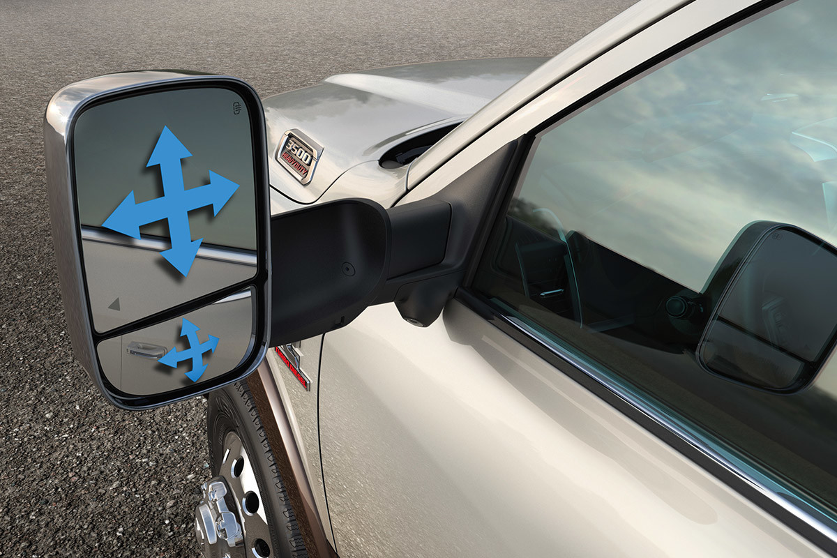 A close-up of two-part trailer tow mirrors on a Bright Silver Metallic coloured 2021 Ram 3500 with illustrated blue arrows showing the convex shape of the mirrors.