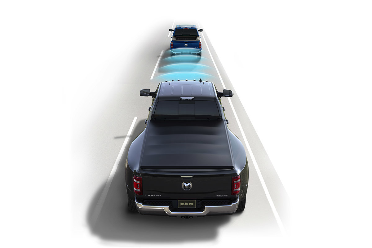 A Granite Crystal Metallic coloured 2021 Ram 3500 with illustrated blue sensor bars emanating from the windshield as it approaches another pickup truck ahead.