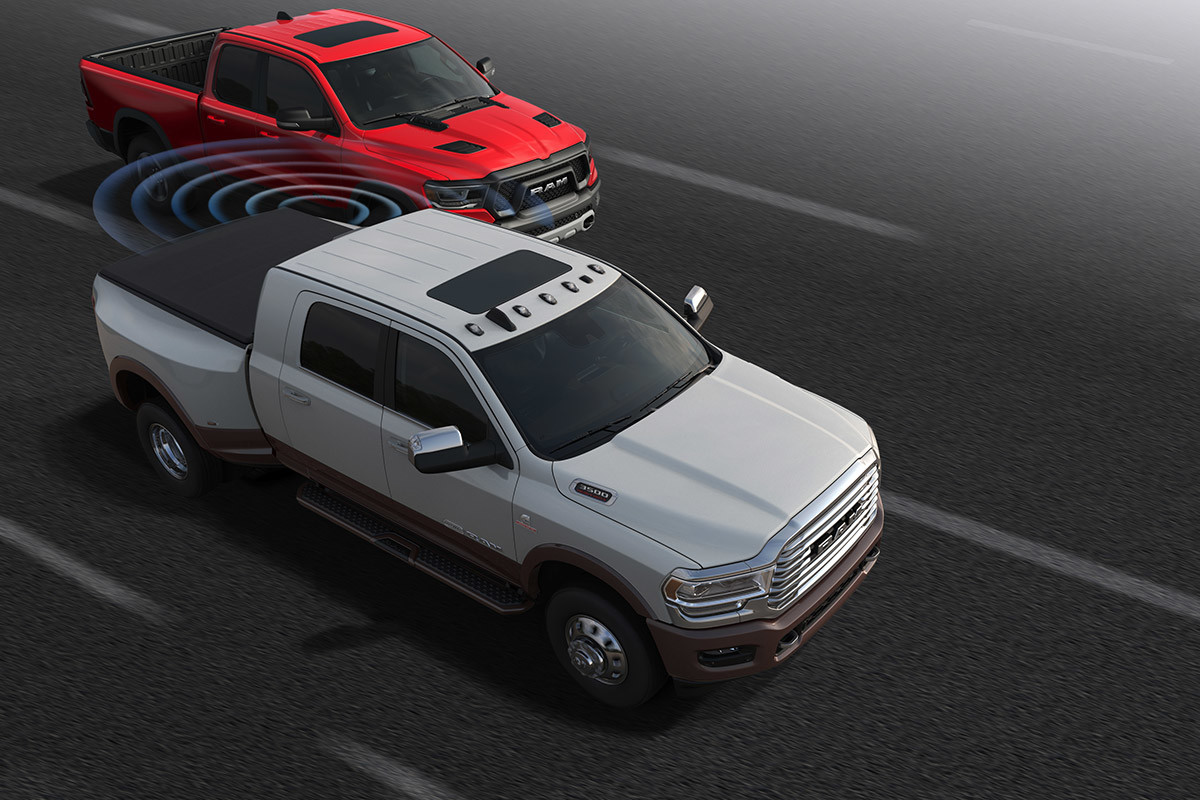 A Bright White coloured 2021 Ram 3500 with illustrated blue sensor bars spanning the space between it and another pickup truck in its blind spot.