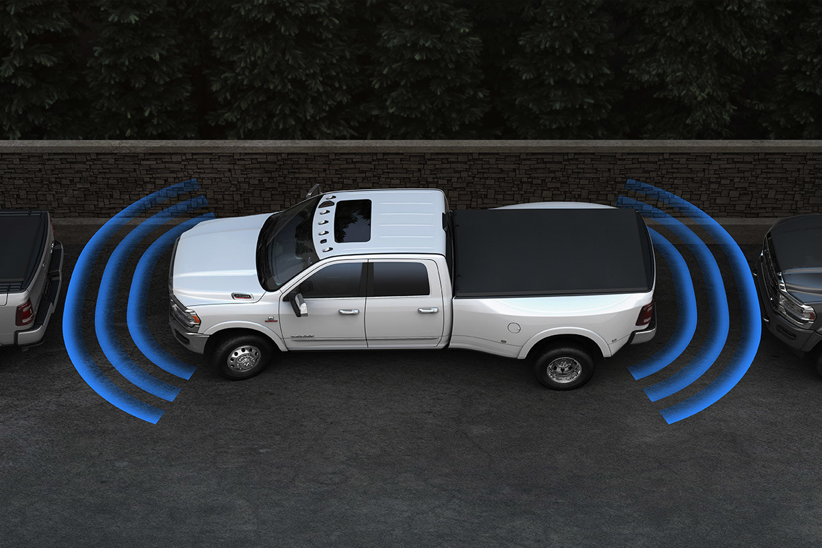 A Bright White coloured 2021 Ram C3500 with a tonneau cover parallel parked at a curb with illustrated blue sensor bars coming from the front and rear of the truck, spanning the space between it and the vehicles in front of it and behind it.