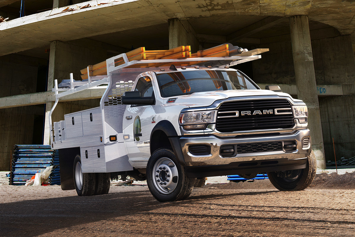 The white 2020 Ram Chassis Cab being driven on a dirt road while ladders on rooftop