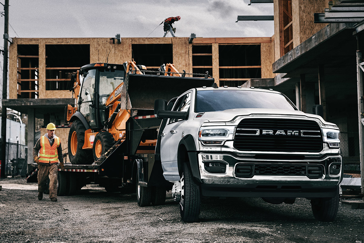 The white 2020 Ram Chassis Cab parked in front of building in a construction site while connected with a payloader