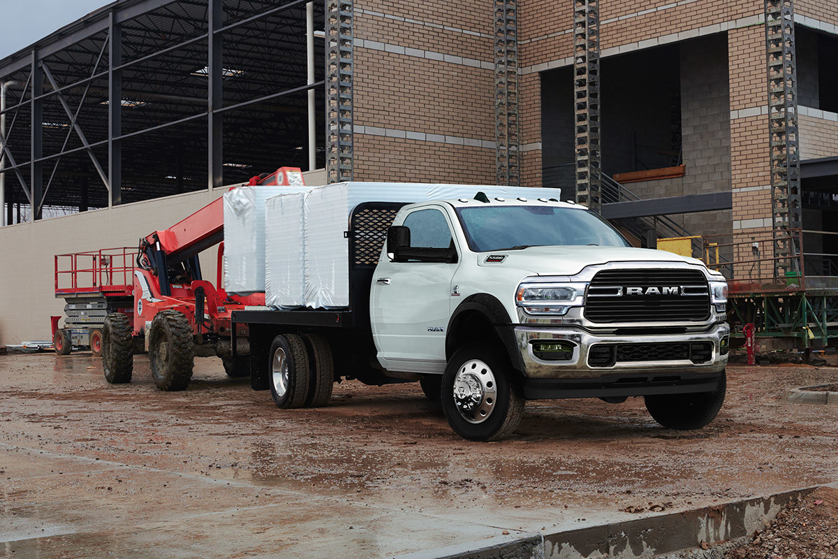 Un châssis-cabine Ram 2021 blanc éclatant amélioré avec un ensemble carrosserie-atelier garé sur un chantier de construction, une nacelle élévatrice garée en arrière.