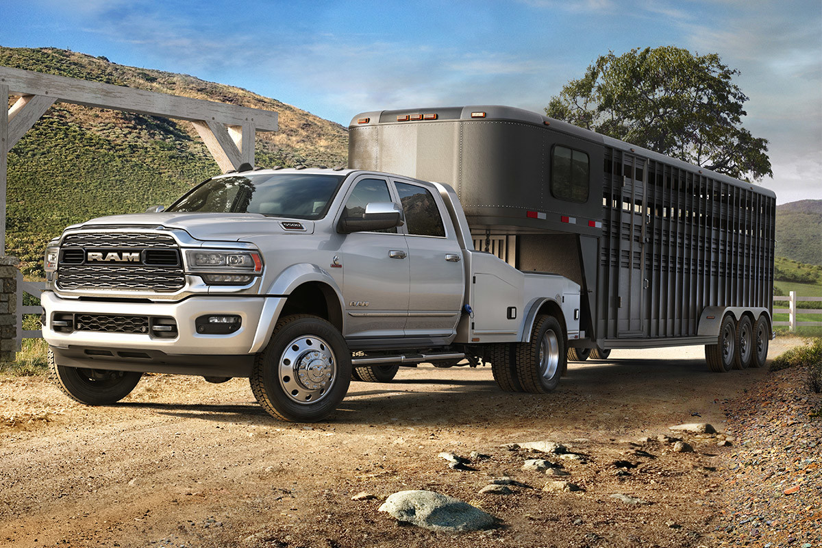 The white 2020 Ram Chassis Cab is towing a trailer on a dirt road