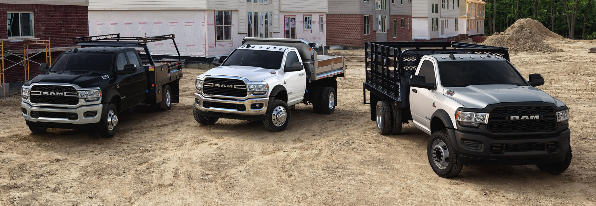Trois modèles de châssis-cabine Ram 2021 améliorés avec différents accessoires de carrosserie-atelier, garés sur un chantier de construction résidentielle.