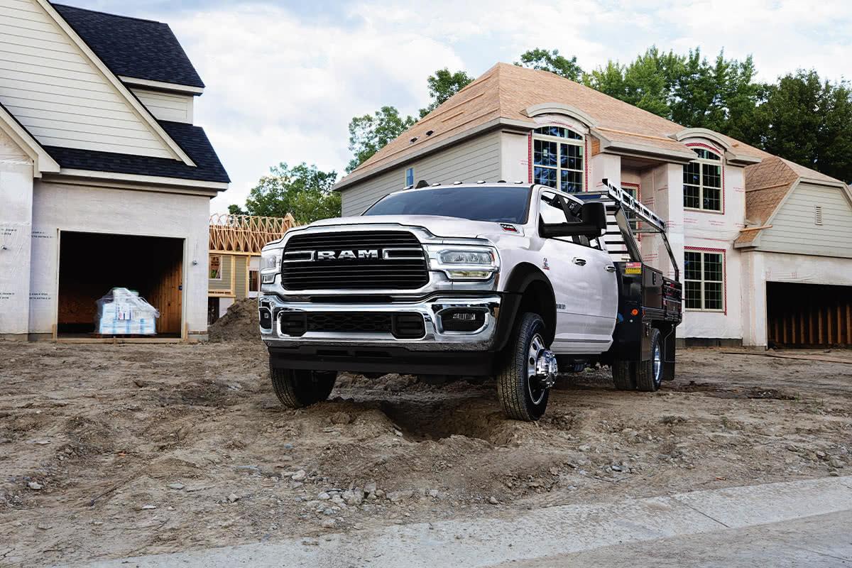 Vue avant d’un châssis-cabine Ram 2021 blanc éclatant amélioré avec un ensemble carrosserie-atelier garé sur un chantier de construction résidentielle.