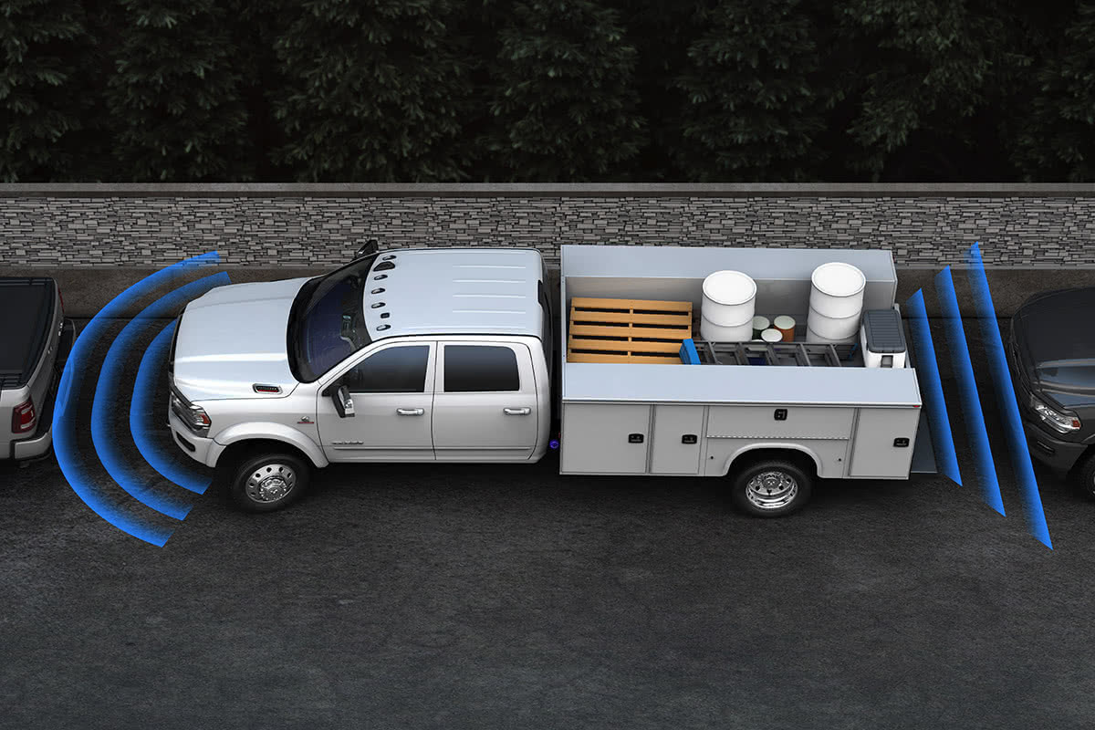 Un châssis-cabine Ram 2021 blanc éclatant avec carrosserie utilitaire stationné en parallèle à un trottoir illustré avec des barres de capteurs bleues à l’avant et à l’arrière du camion, couvrant l’espace avec les véhicules qui l’entourent.