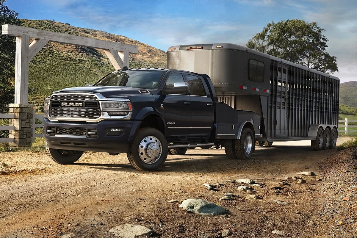 Vue latérale d’un châssis-cabine Ram 2021 couche nacrée cristal noir étincelant tractant une remorque à chevaux sur la route d’un ranch.