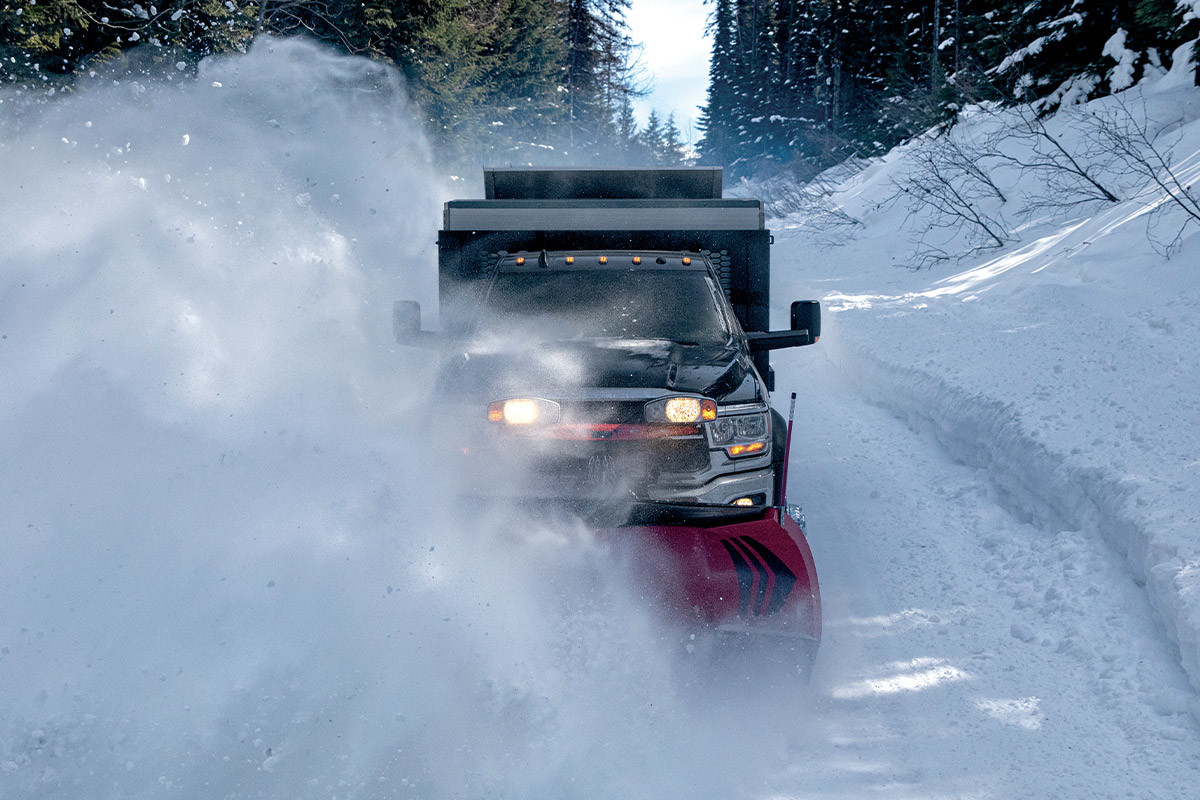 Un Ram châssis-cabine 2022 noir équipé d’un chasse-neige à l’avant, déneigeant la route.