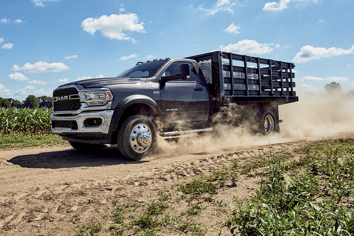 A Patriot Blue Pearl 2022 Ram Chassis Cab being driven on a dirt road through farm fields.