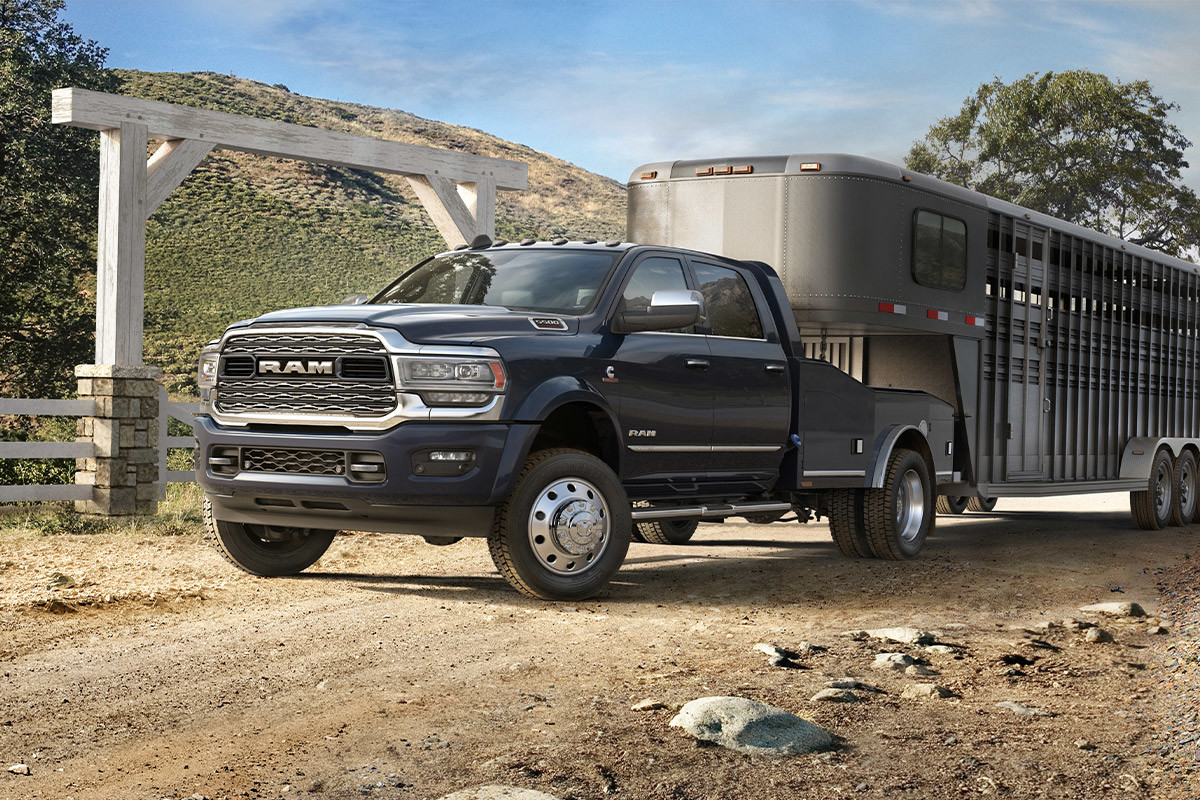 A side view of a Diamond Black Crystal Pearl 2022 Ram Chassis Cab towing a horse trailer on a ranch road.