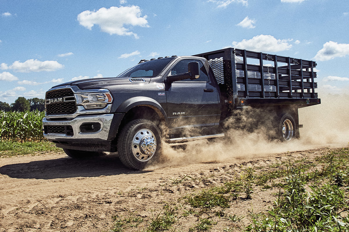 A Patriot Blue Pearl 2022 Ram Chassis Cab being driven on a dirt road through farm fields.