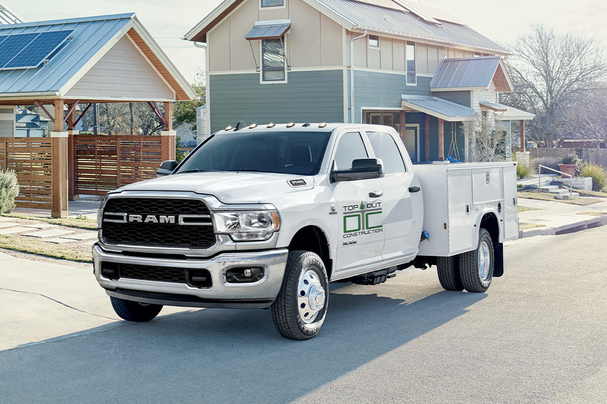 2022 3500 Chassis Cab SLT in Bright White with Utility Box upfit and dual rear wheels, parked on a paved street next to houses under construction.