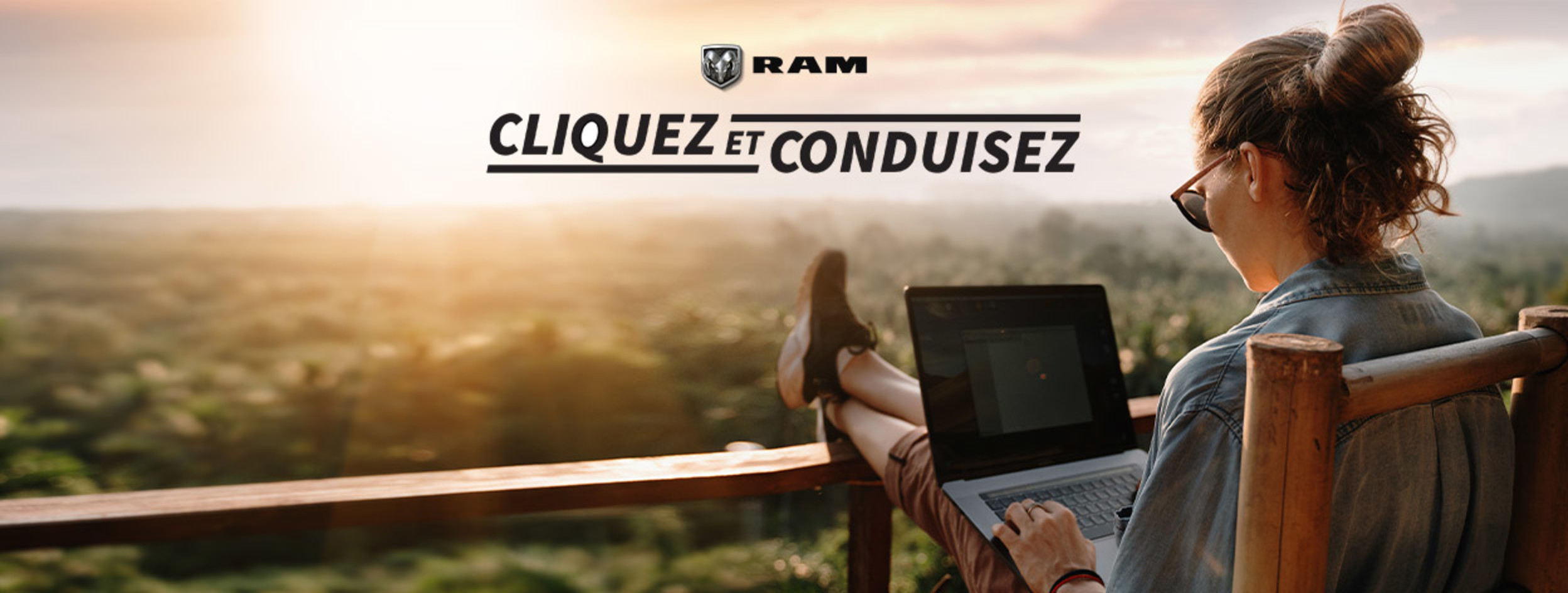 Une personne sur son ordinateur portable, assise sur une chaise en bois sur un balcon donnant sur une forêt.