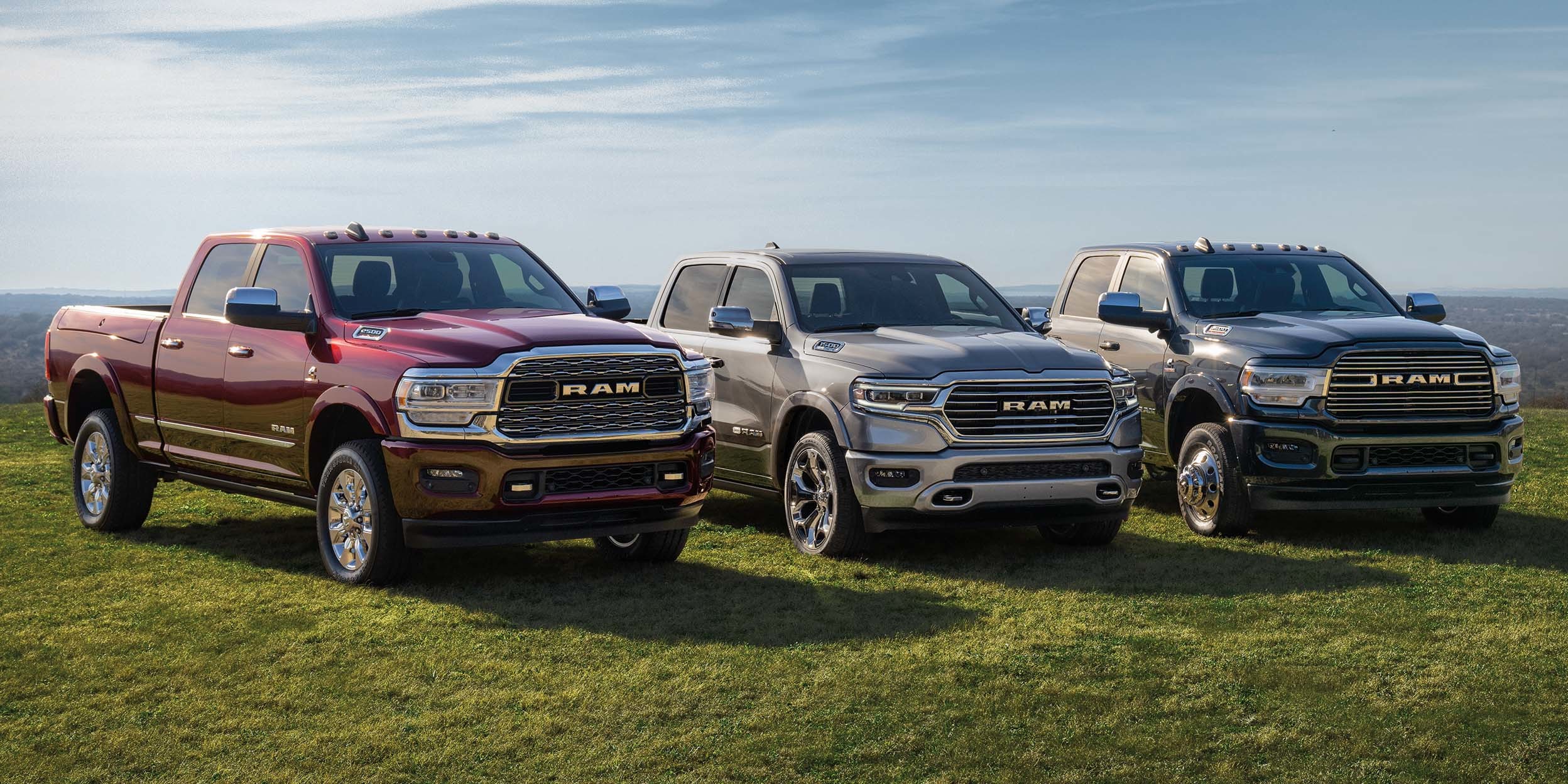2500 Limited in Red Pearl and 3500 Limited in Brilliant Black Crystal Pearl and 1500 in silver parked on terrain with mountains in the distance.