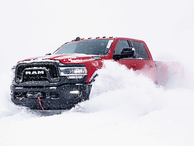Ram HD rouge roulant sur un sentier enneigé et soulevant de la neige en se déplaçant. L’arrière-plan est blanc avec une visibilité limitée.