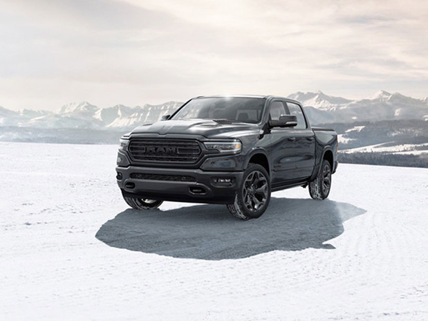 Vue d'un Ram 1500 2023 noir stationné au sommet d'un chemin couvert de neige avec des montagnes derrière.