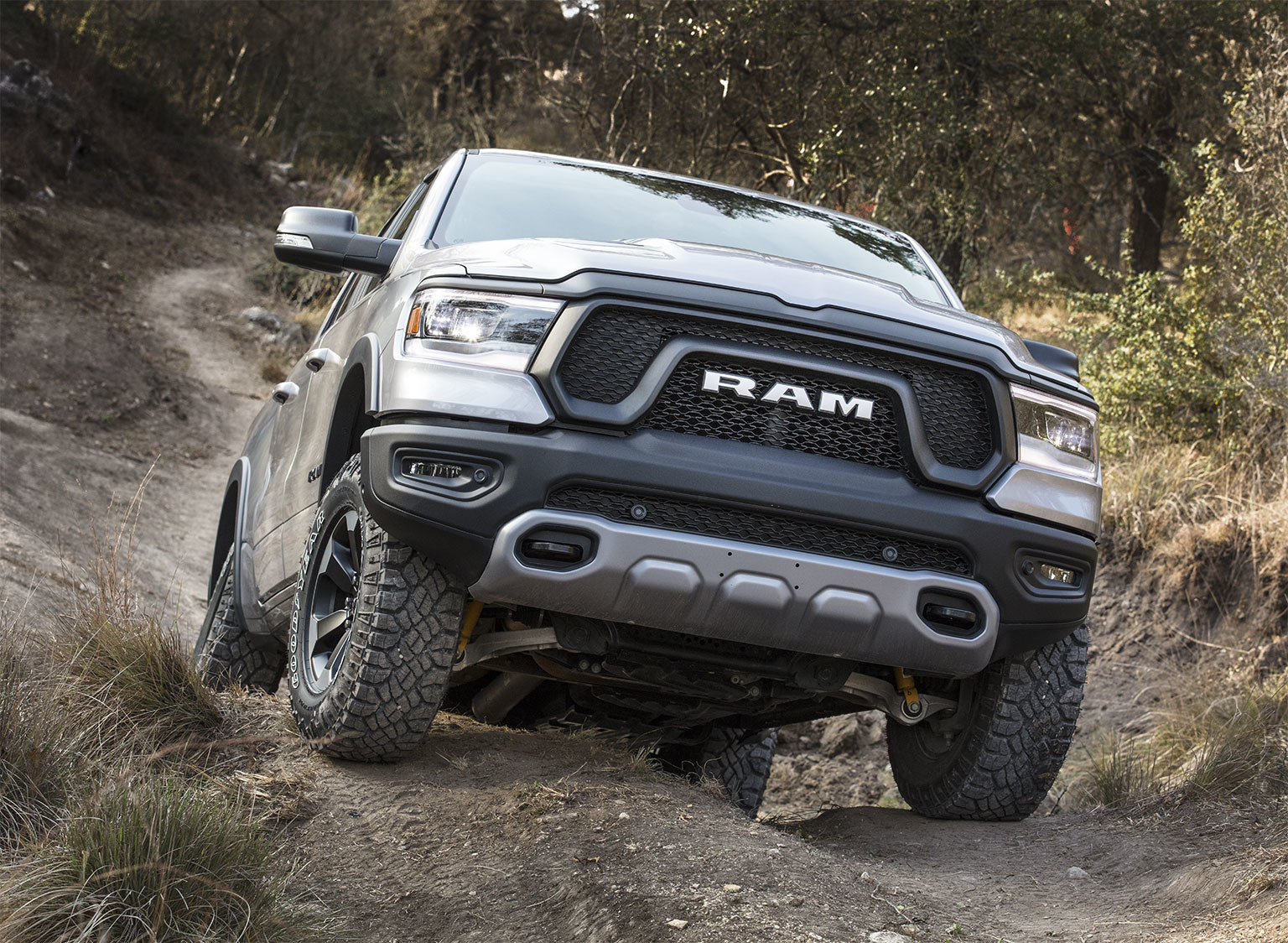 A silver Ram 1500 being driven up a steep, dirt road, through a forest.