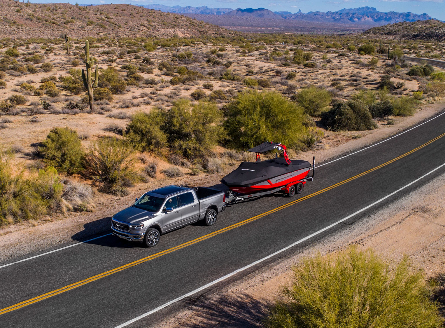 Un Ram 1500 gris conduit sur une route et tirant un bateau. A grey Ram 1500 being driven down a road and pulling a boat.