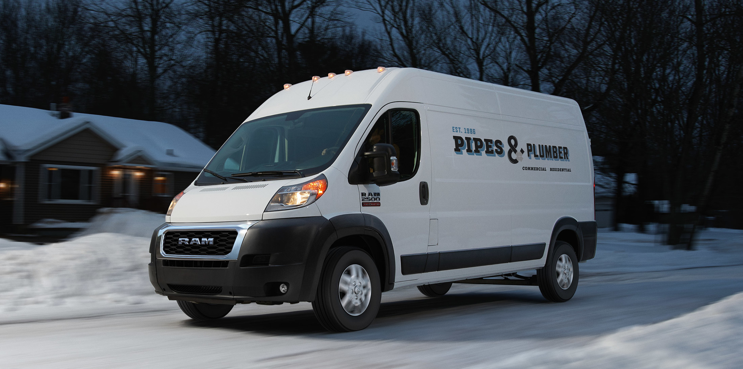 White Ram ProMaster driving down a snowy, residential road with bare trees in the background.