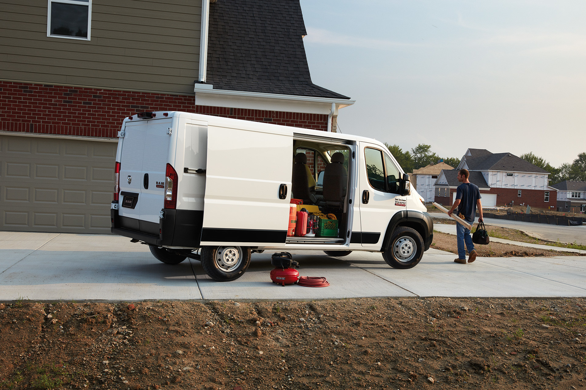 Le Ram ProMaster 2020 blanc stationné dans une entrée près d’une maison, porte latérale ouverte