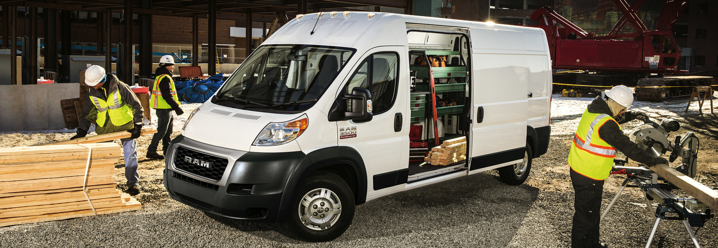 Ram ProMaster parked on a construction site with the side door open and equipment inside. Three construction workers are working nearby.