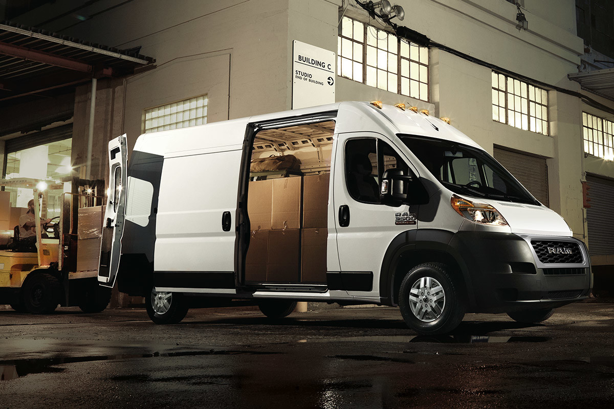 Ram ProMaster stationné à proximité d’un bâtiment avec la porte du véhicule ouverte et plusieurs caisses empilées à l’intérieur.