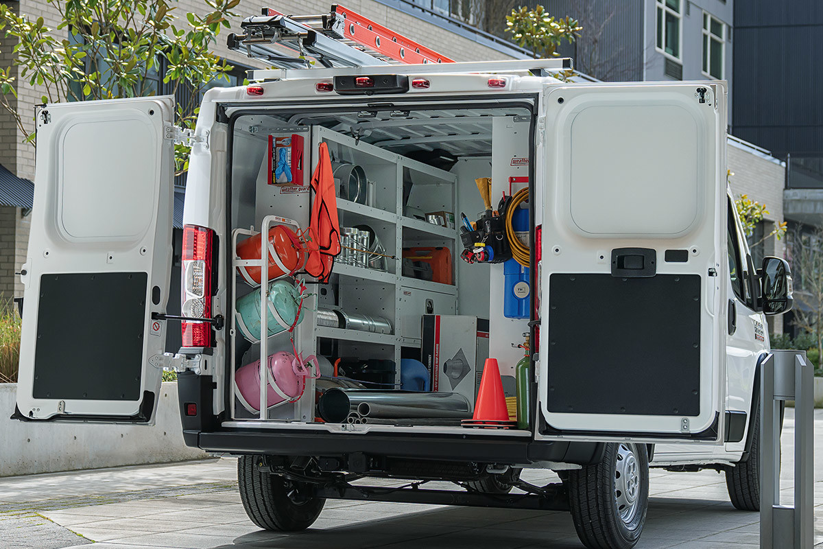 Ram ProMaster parked on a street by condo buildings has its rear doors open, revealing equipment inside.
