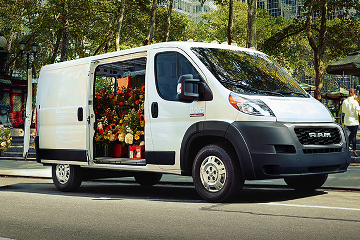 Ram ProMaster parked on a street with side door open revealing lots of flower bouquets inside, while people set up for an event in the background.