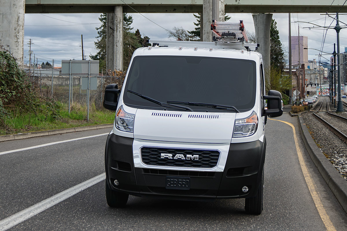 Ram ProMaster driving on a road, with a bridge and city buildings in the background.