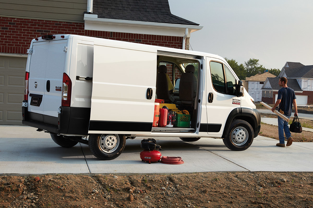 Ram ProMaster stationné à proximité d’une maison. La porte latérale ouverte laisse entrevoir un homme déchargeant du matériel.