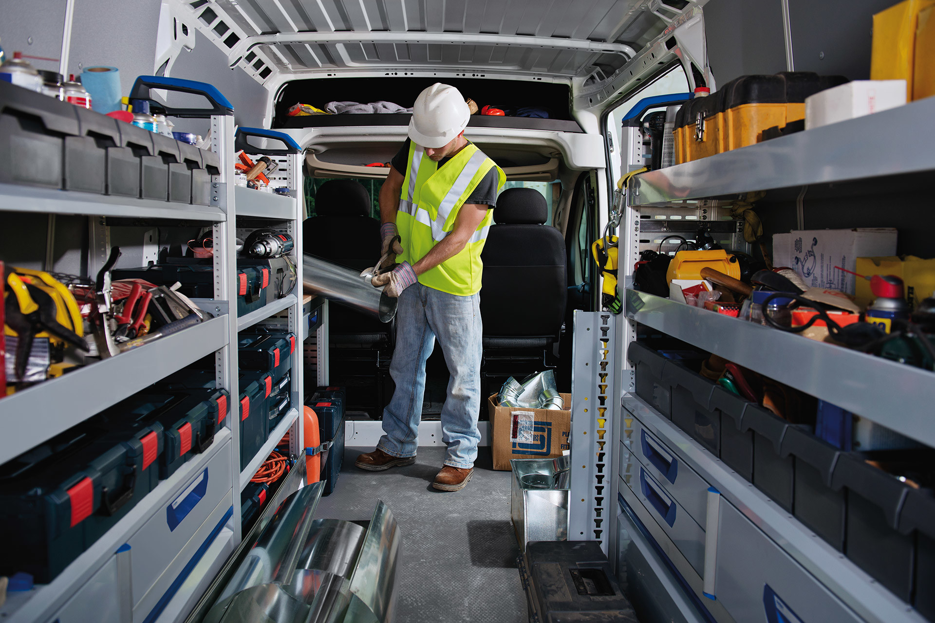 Vue intérieure du Ram ProMaster présentant du matériel de construction disposé dans un rayonnage configurable, avec un ouvrier se tenant debout à l’intérieur.