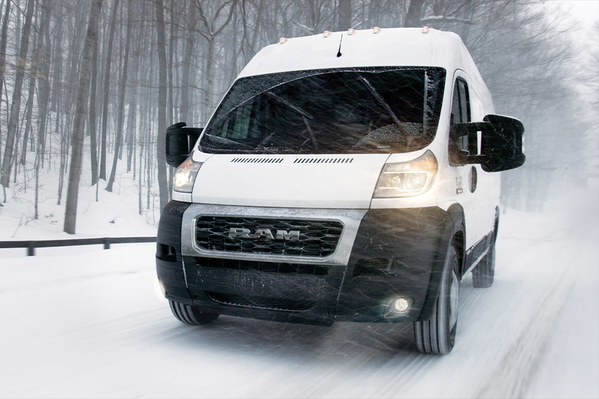 Vue de face d’un Ram ProMaster 2022, illustré en blanc, roulant dans la neige avec des arbres en arrière-plan.