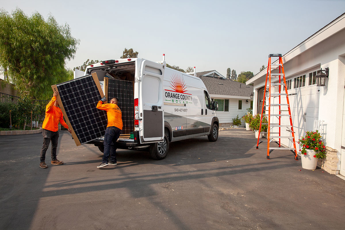 Vue arrière d'un Ram ProMaster 2023 blanc avec deux travailleurs en chemises orange déchargeant un gros meuble.