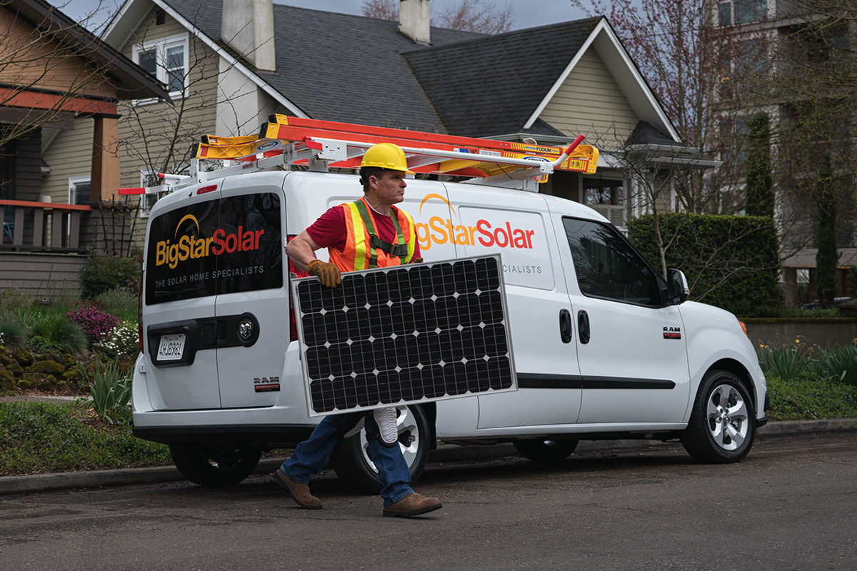 Man in construction uniform walking by 2020 Ram ProMaster City parked on a road in front of a house