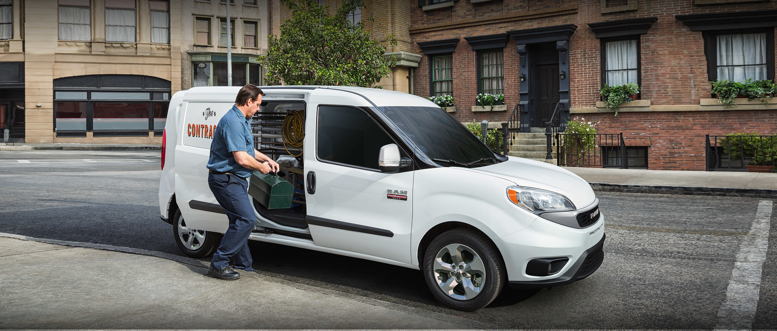 Un Ram ProMaster City 2020 stationné dans une zone urbaine pendant qu’un homme charge une boîte à outils