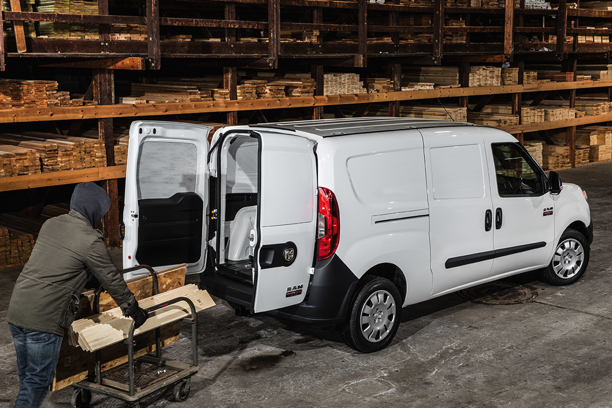 Ram ProMaster City 2021 blanc garé dans une cour à bois. Un homme est en train de charger du bois dans l’espace utilitaire arrière.