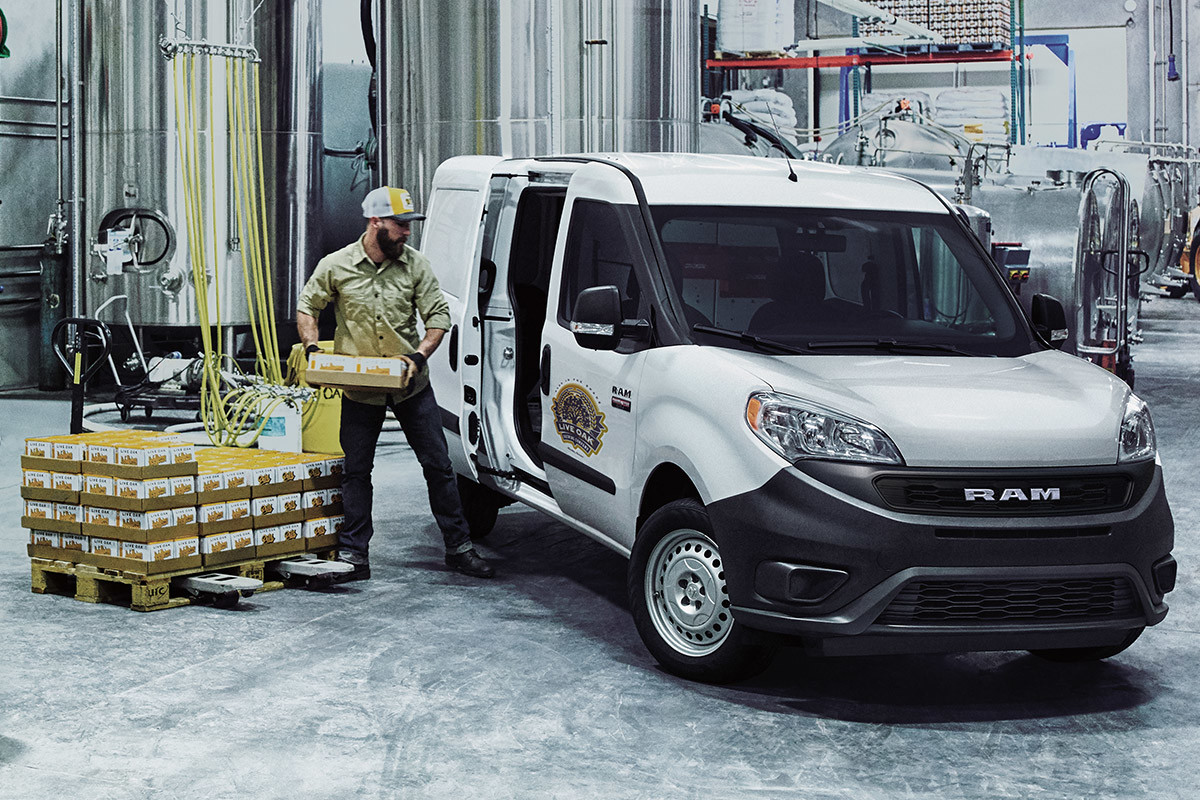 Ram ProMaster City 2021 blanc garé dans une brasserie. Un ouvrier charge des paquets par la porte latérale.