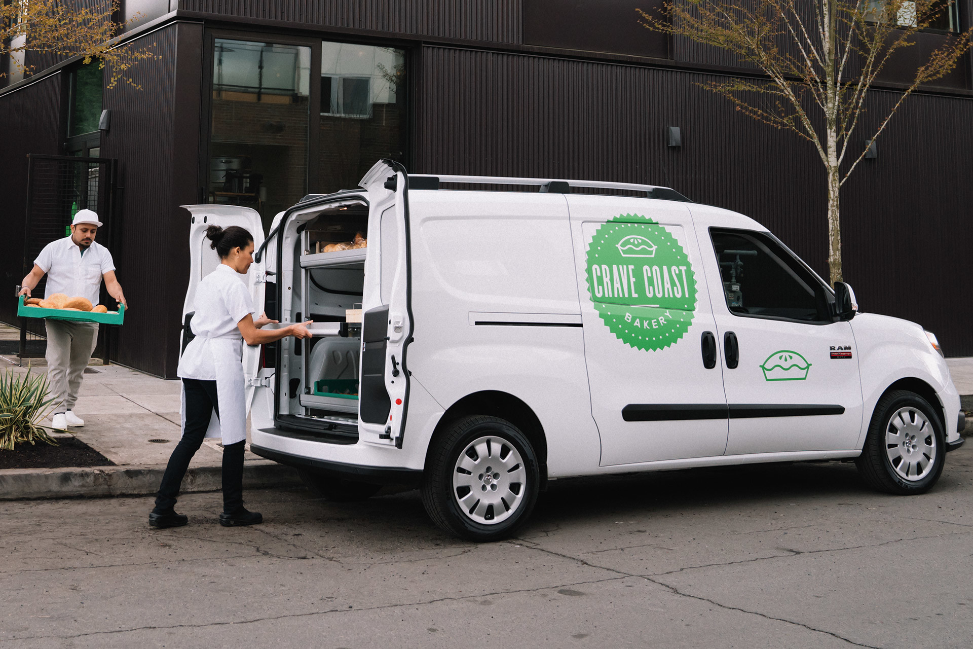 White 2021 Ram ProMaster City parked with the rear doors open. Two caterers are loading it with food.