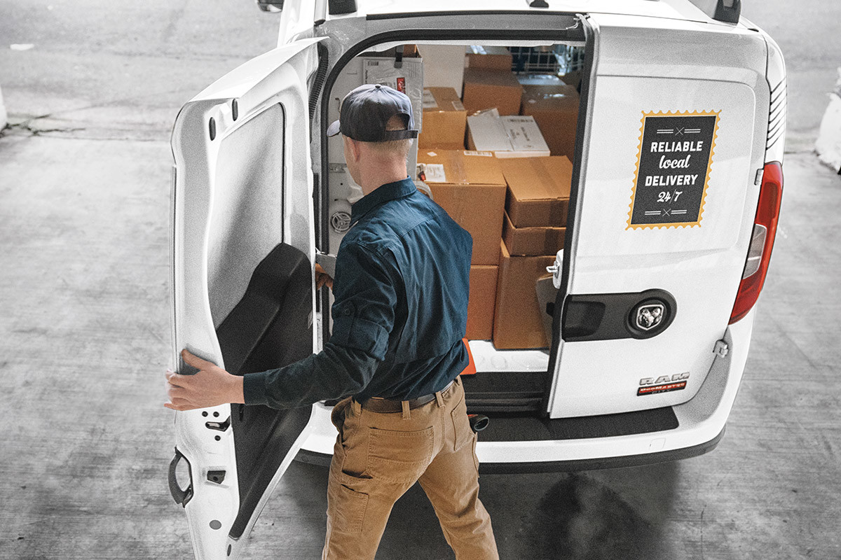 A person closing the rear door of a white 2022 Ram ProMaster City.