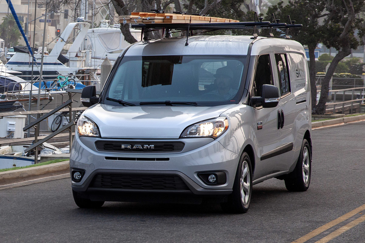 Un Ram ProMaster City argenté 2022 conduit sur une route avec des bateaux en arrière-plan.