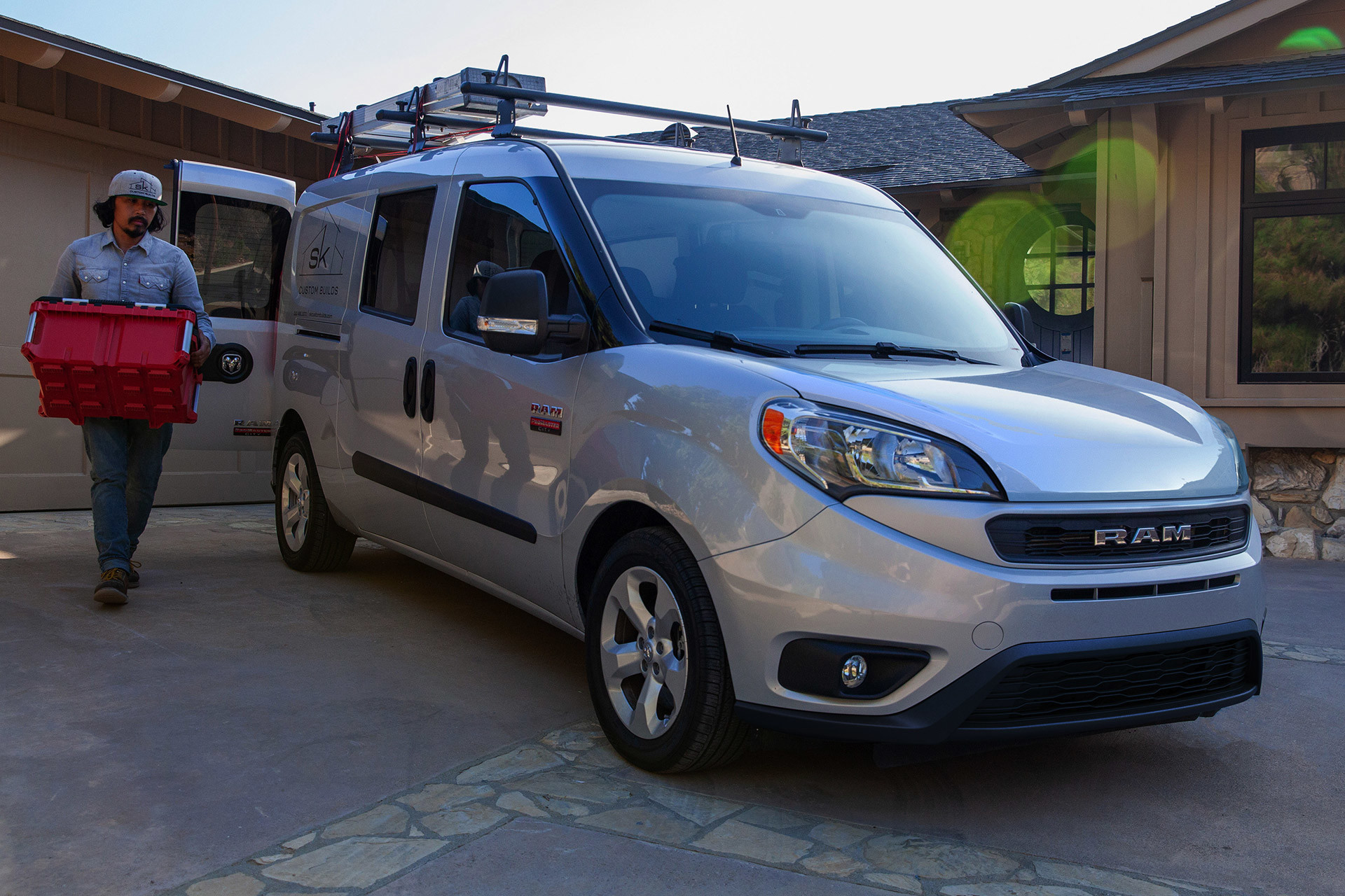 Une personne déchargeant un sac d'un Ram ProMaster City 2022 argent garé.